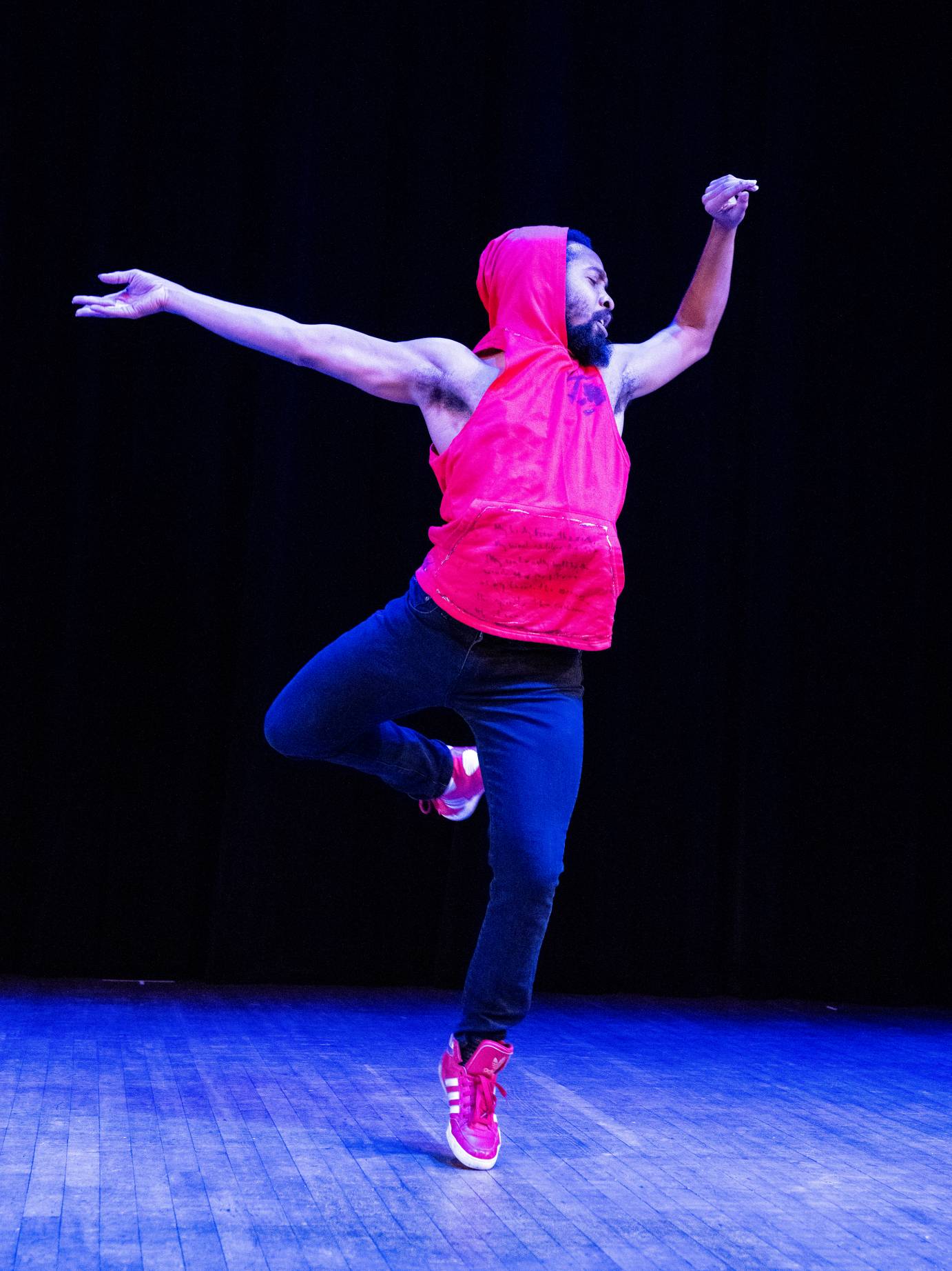 artist Johnnie Cruise Mercer in a translike dance. He wears a sleevless red hoodie, jeans and red sneaker 